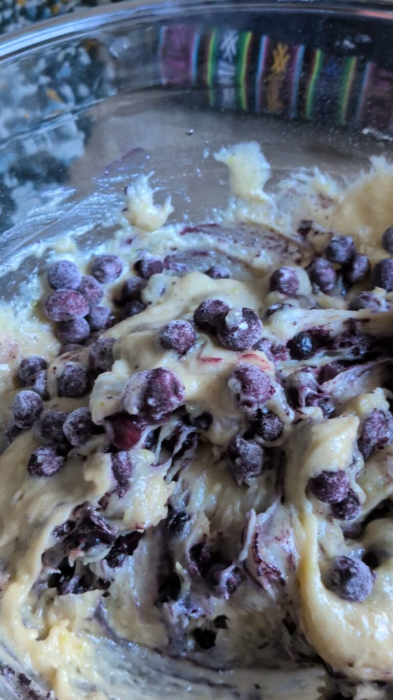 Freshly baked blueberry muffins made with oil, golden tops, vibrant bursts of blueberries, soft fluffy texture, muffins cooling on a rack, natural light, home-baked breakfast treat.