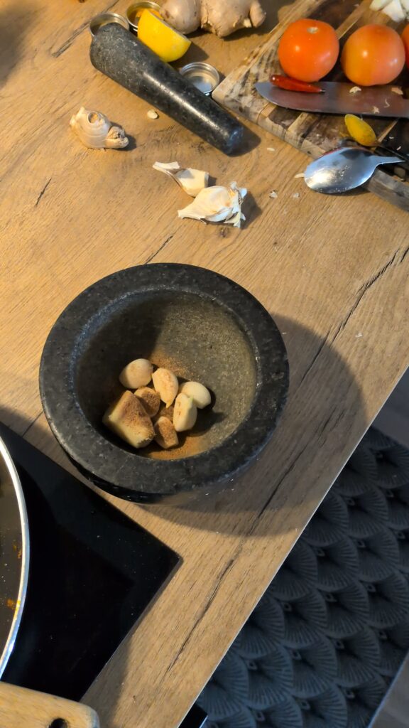 Nepali chicken curry in a traditional bowl with fresh cilantro and scallion garnish, Close-up of bone-in chicken pieces in thick tomato gravy, Step-by-step frying chicken in a heavy-bottomed pan with spices, Grinding ginger-garlic with powdered spices in a mortar and pestle, Adding tomatoes and ground spices to the chicken curry, Finished Nepali chicken curry served with steamed rice and roti, Garnishing chicken curry with fresh cilantro and scallions, Nepali Chicken Curry (Kukhura Ko Masu) – A Home-Style Recipe From My Roots, saru's diary, saru's not so secret diary, nepali food , nepali food blog, food around the world, chicken recipes around the world