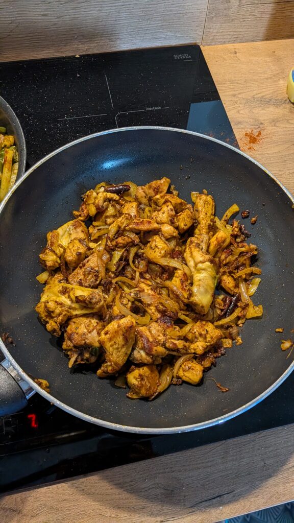 Nepali chicken curry in a traditional bowl with fresh cilantro and scallion garnish, Close-up of bone-in chicken pieces in thick tomato gravy, Step-by-step frying chicken in a heavy-bottomed pan with spices, Grinding ginger-garlic with powdered spices in a mortar and pestle, Adding tomatoes and ground spices to the chicken curry, Finished Nepali chicken curry served with steamed rice and roti, Garnishing chicken curry with fresh cilantro and scallions, Nepali Chicken Curry (Kukhura Ko Masu) – A Home-Style Recipe From My Roots, saru's diary, saru's not so secret diary, nepali food , nepali food blog, food around the world, chicken recipes around the world